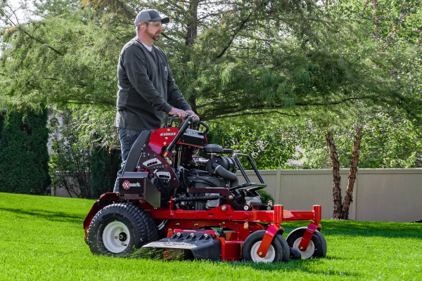 Man standing on back of riding lawn mower